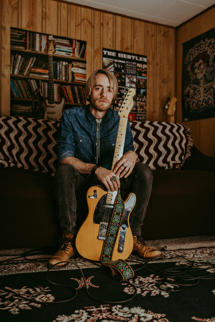 Jay Bowcott holding a guitar in a basement