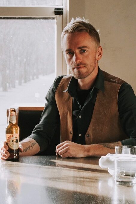 Jay Bowcott in front of a window sitting at a Table with a bottle